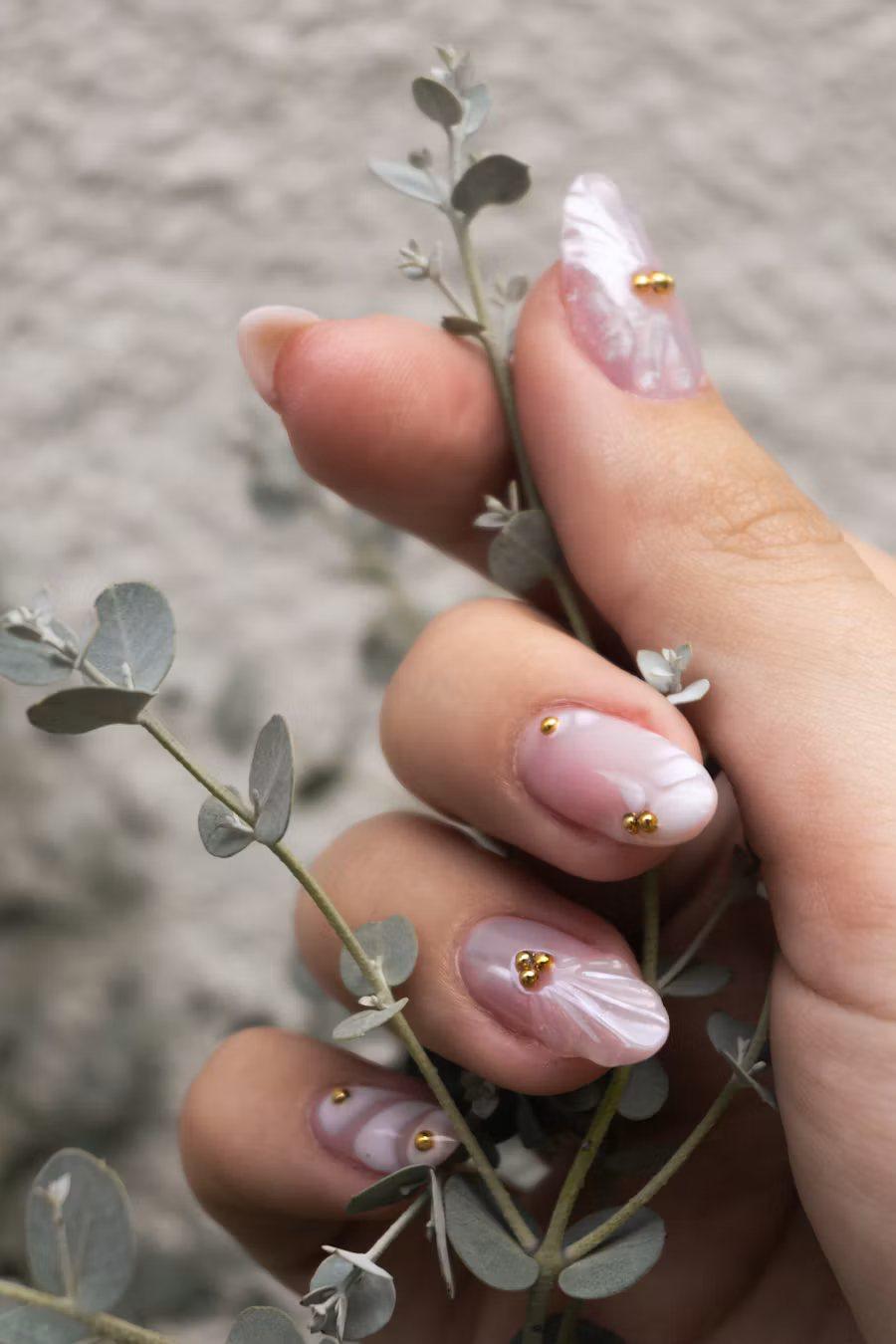 Hand holding eucalyptus, with pearly pink almond nails and tiny gold beads