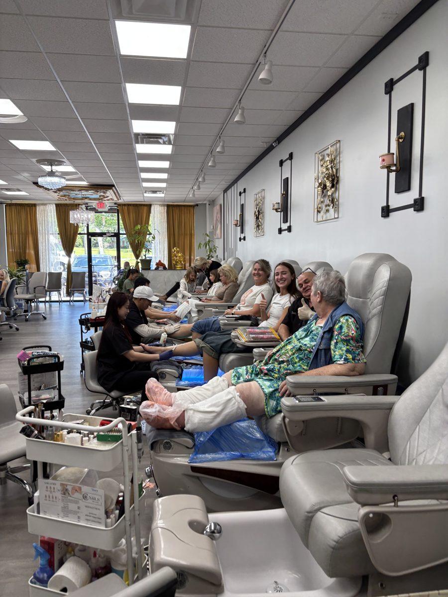Inside C Nails & Spa: a row of pedicure chairs along a wall with gold decor, and nail technicians at work